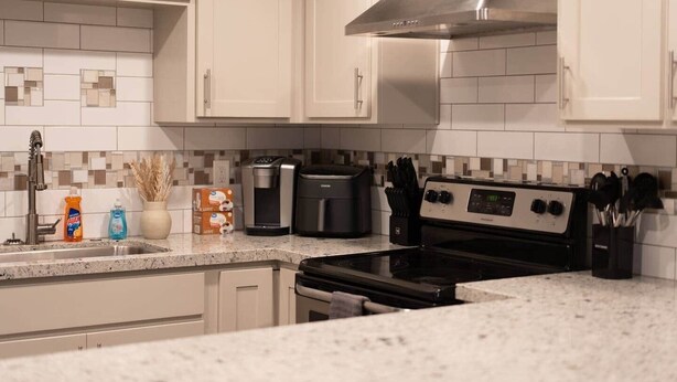 A modern kitchen with white cabinets, a stainless steel range hood, a coffee maker, a toaster, and a stove. - Kipps Hill Haven B — Folsom Lake Escape (El Dorado Hills)