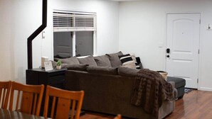 A living room with a sofa, a dining table, and chairs. There is a window with blinds, a door, and a small table with a plant. - Kipps Hill Haven B — Folsom Lake Escape (El Dorado Hills)