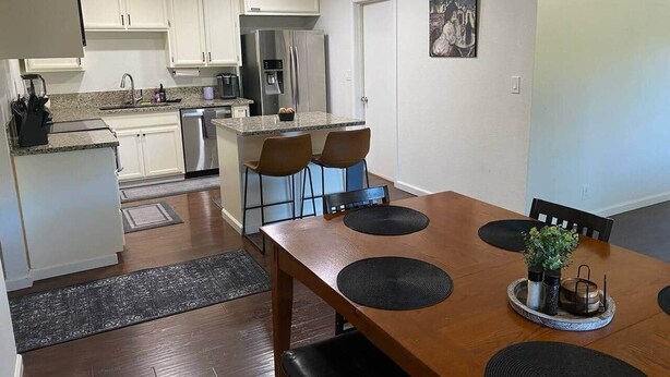 A modern kitchen with white cabinets, a stainless steel refrigerator, and a dining area with a wooden table and chairs.