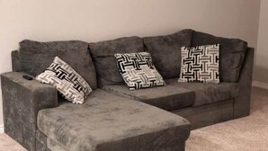 Un sofá seccional gris con tres almohadones estampados y un control remoto encima.