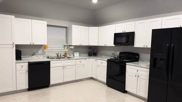 Una cocina moderna con armarios blancos, un refrigerador negro, un microondas y un lavavajillas.