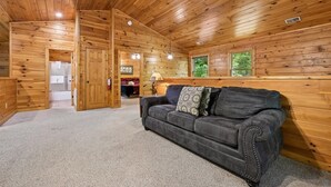 L’intérieur d’une cabane en rondins, avec un canapé en cuir, des murs en bois et un plancher recouvert de moquette.