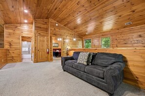 A log cabin interior with a leather sofa, wooden walls, and a carpeted floor. - Spacious Cabin w/ Game Room, Hot Tub & Fireplace (Gatlinburg)