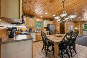 A wooden cabin interior with a kitchen, dining area, and a chandelier. - Spacious Cabin w/ Game Room, Hot Tub & Fireplace (Gatlinburg)