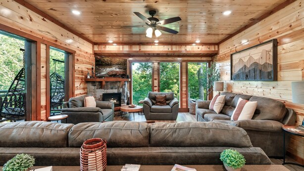 A cozy cabin interior with a large couch, two armchairs, a fireplace, and a dining area. - Glorious Mountain Lodge w/ Pool, Theater & Hot Tub (Gatlinburg)