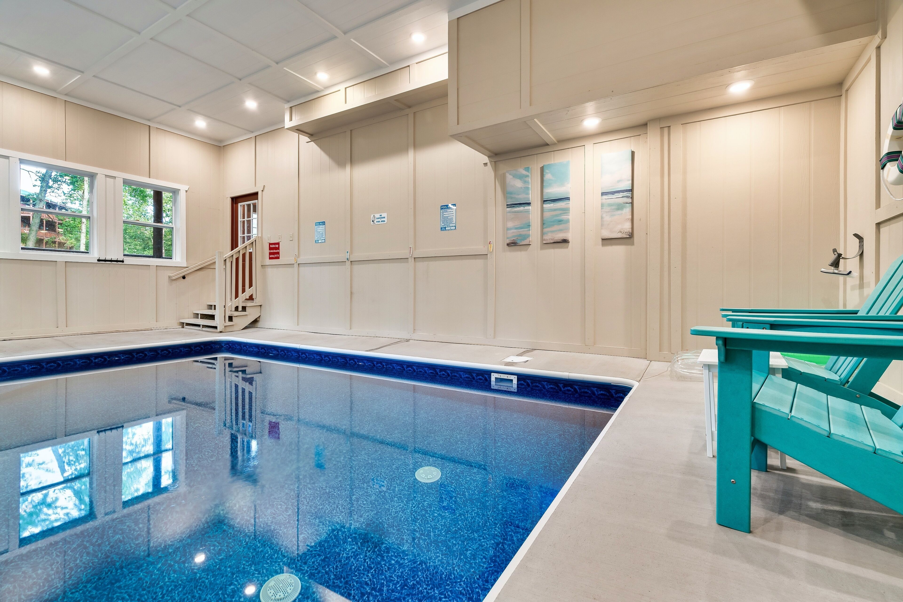 A swimming pool with a clear blue water, a staircase, and a teal chair.