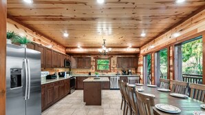A spacious kitchen with wooden cabinets, a stainless steel refrigerator, and a dining area with a wooden table and chairs. - Glorious Mountain Lodge w/ Pool, Theater & Hot Tub (Gatlinburg)