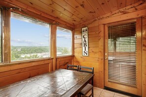 A cabin interior with a wooden table, chairs, a window with a view, and a door with a sign. - Luxury Mountain Retreat w/ Hot Tub & Views (Pigeon Forge)