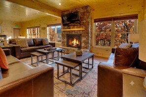 Ein gemütliches Lodge-Interieur mit Kamin aus Stein, Ledermöbeln und großen Fenstern.