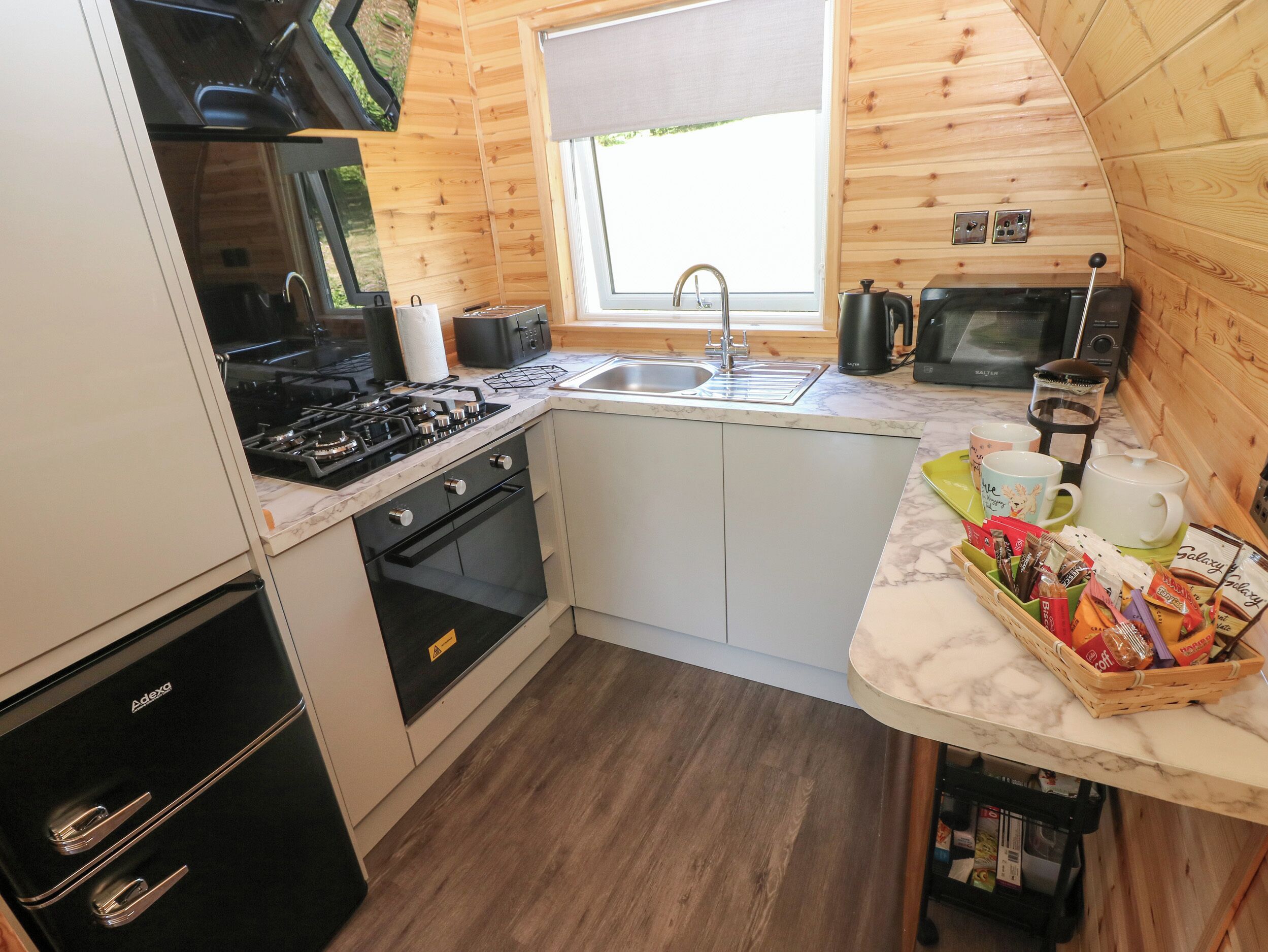 A compact kitchen with a gas stove, oven, sink, and a window above the sink.