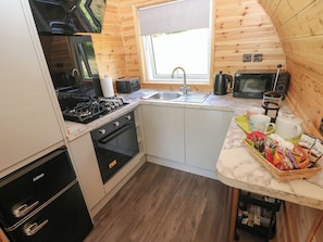 A compact kitchen with a gas stove, oven, sink, and a window above the sink.