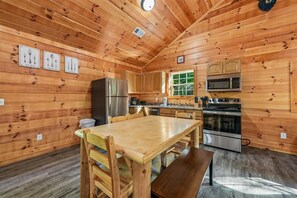 A wooden cabin interior with a dining table, chairs, a refrigerator, a microwave, and a stove. - Cozy Cabin w/ Fire Pit & Hot Tub (Pigeon Forge)