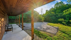 Un espace extérieur abrité, doté d’un sol en béton, de poutres en bois et offrant une vue sur une route et la verdure.