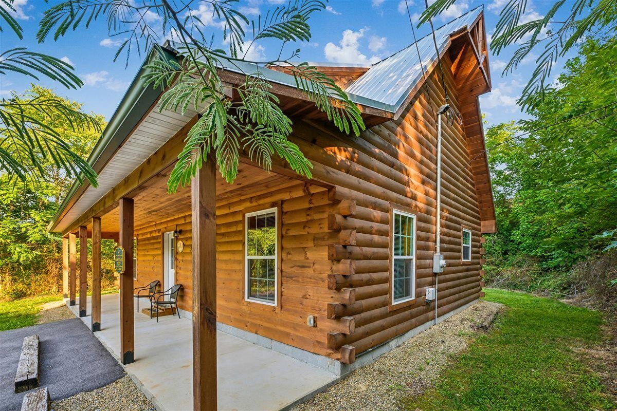 A log cabin with a porch, two windows, and a covered outdoor seating area.