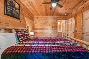 A wooden cabin room with a bed, a ceiling fan, and a framed picture on the wall. - Cozy Cabin w/ Fire Pit & Hot Tub (Pigeon Forge)