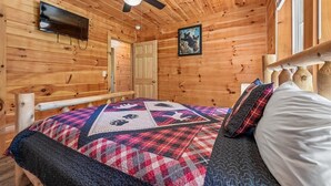 L’intérieur d’une cabane en bois, avec un lit, un ventilateur de plafond, un téléviseur fixé au mur et une porte.
