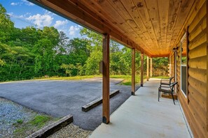 A covered porch with a concrete floor, wooden pillars, and a view of a road and greenery. - Cozy Cabin w/ Fire Pit & Hot Tub (Pigeon Forge)