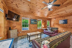 Ein Holzblockbau-Innenraum mit Fernseher, Sofa und Deckenventilator.