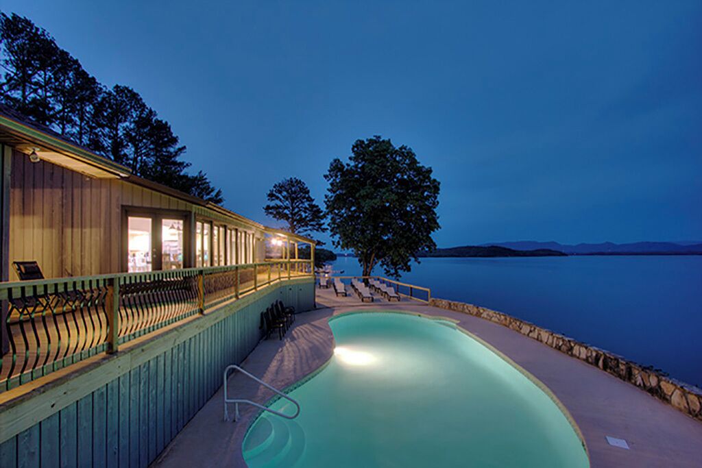 A swimming pool with a wooden deck and lounge chairs, overlooking a body of water.