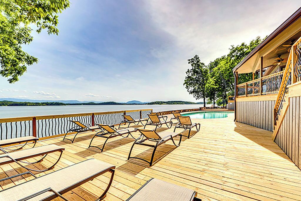 A wooden deck with lounge chairs and a pool area, overlooking a body of water.