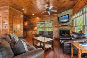 A cozy cabin interior with wooden walls, a fireplace, leather sofas, and a television mounted on the wall. - Chic Cabin w/ Theater & Fireplaces (Sevierville)