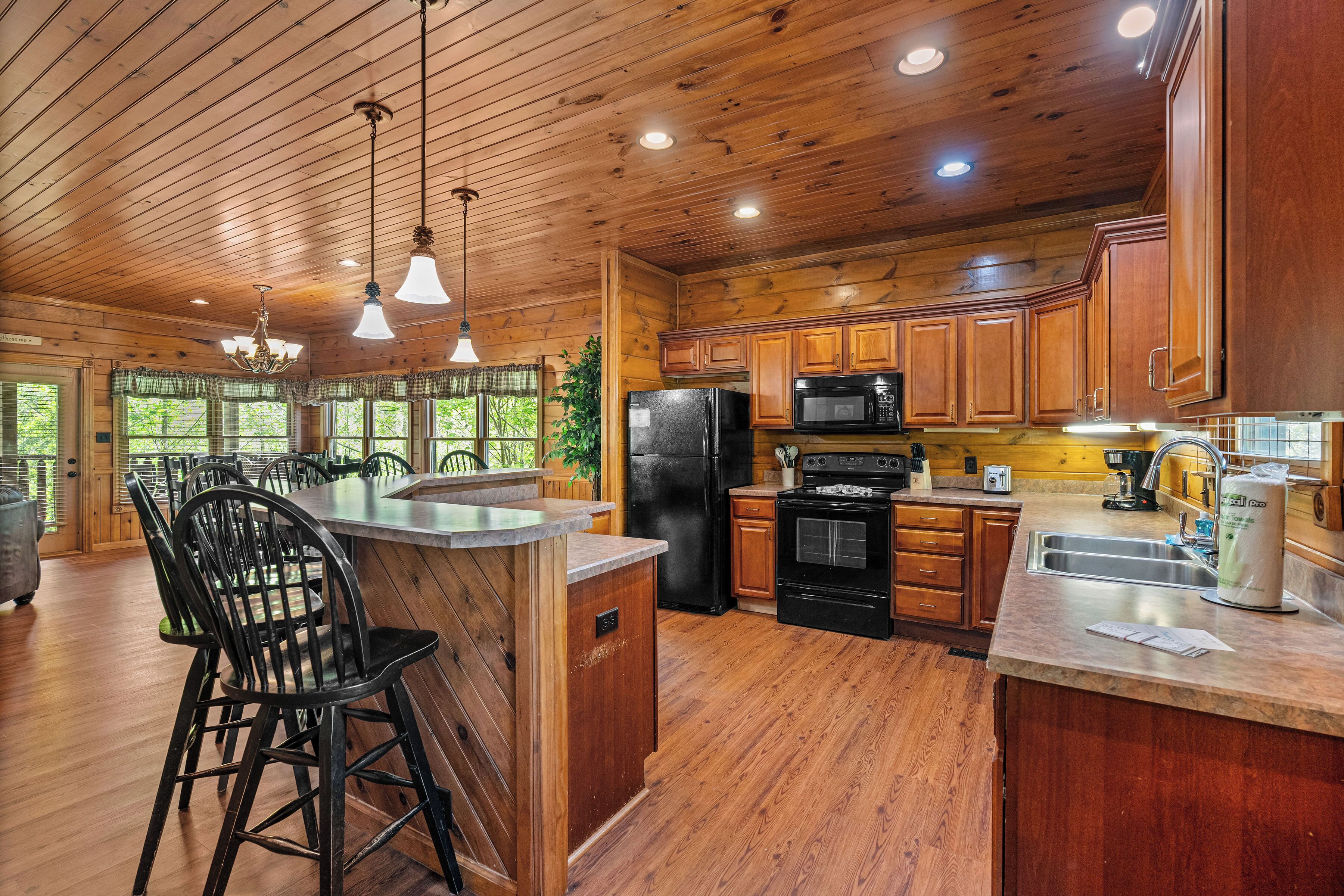 A wooden cabin interior with a kitchen featuring a refrigerator, stove, microwave, and bar area.