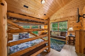 A cabin interior with a bunk bed, a sofa, a lamp, and a television. - Premier Riverfront Retreat w/ Hot Tub & Games (Pigeon Forge)