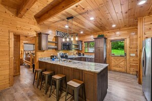 A wooden cabin interior with a kitchen featuring a marble countertop, bar stools, and a sign that reads 'LET'S FEED'. - Premier Riverfront Retreat w/ Hot Tub & Games (Pigeon Forge)
