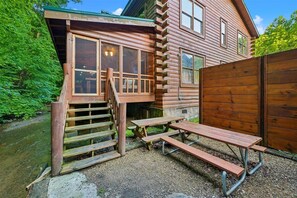 A rustic cabin with a wooden exterior, a porch, and a picnic table. - Premier Riverfront Retreat w/ Hot Tub & Games (Pigeon Forge)