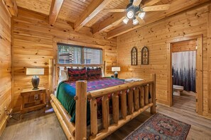 Ein Schlafzimmer einer Holzhütte mit einem Bett, zwei Nachttischen, einem Deckenventilator und einem Fenster mit Jalousien.