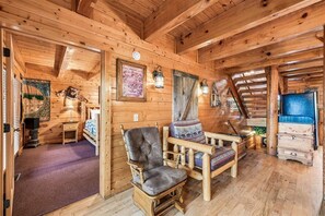 A wooden cabin interior with a loft bed, a cushioned chair, and a small table. - Majestic Lodge w/ Views, Hot Tub & Games (Sevierville)