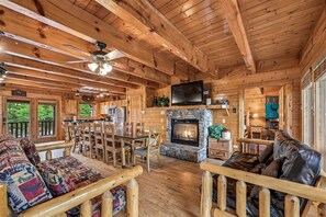 A log cabin interior with a fireplace, dining area, and seating. - Majestic Lodge w/ Views, Hot Tub & Games (Sevierville)