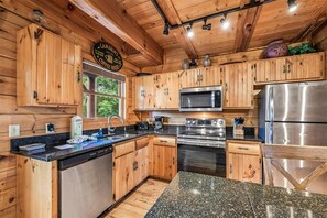 A wooden cabin interior with a kitchen featuring wooden cabinets, a microwave, a refrigerator, and a dishwasher. - Majestic Lodge w/ Views, Hot Tub & Games (Sevierville)