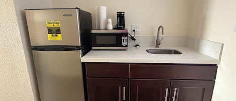 Una cocina compacta equipada con un refrigerador de acero inoxidable, un microondas, una cafetera y un lavamanos.