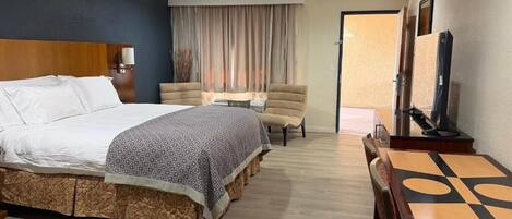 A hotel room with a large bed, a desk, a chair, a TV, and a window with curtains.