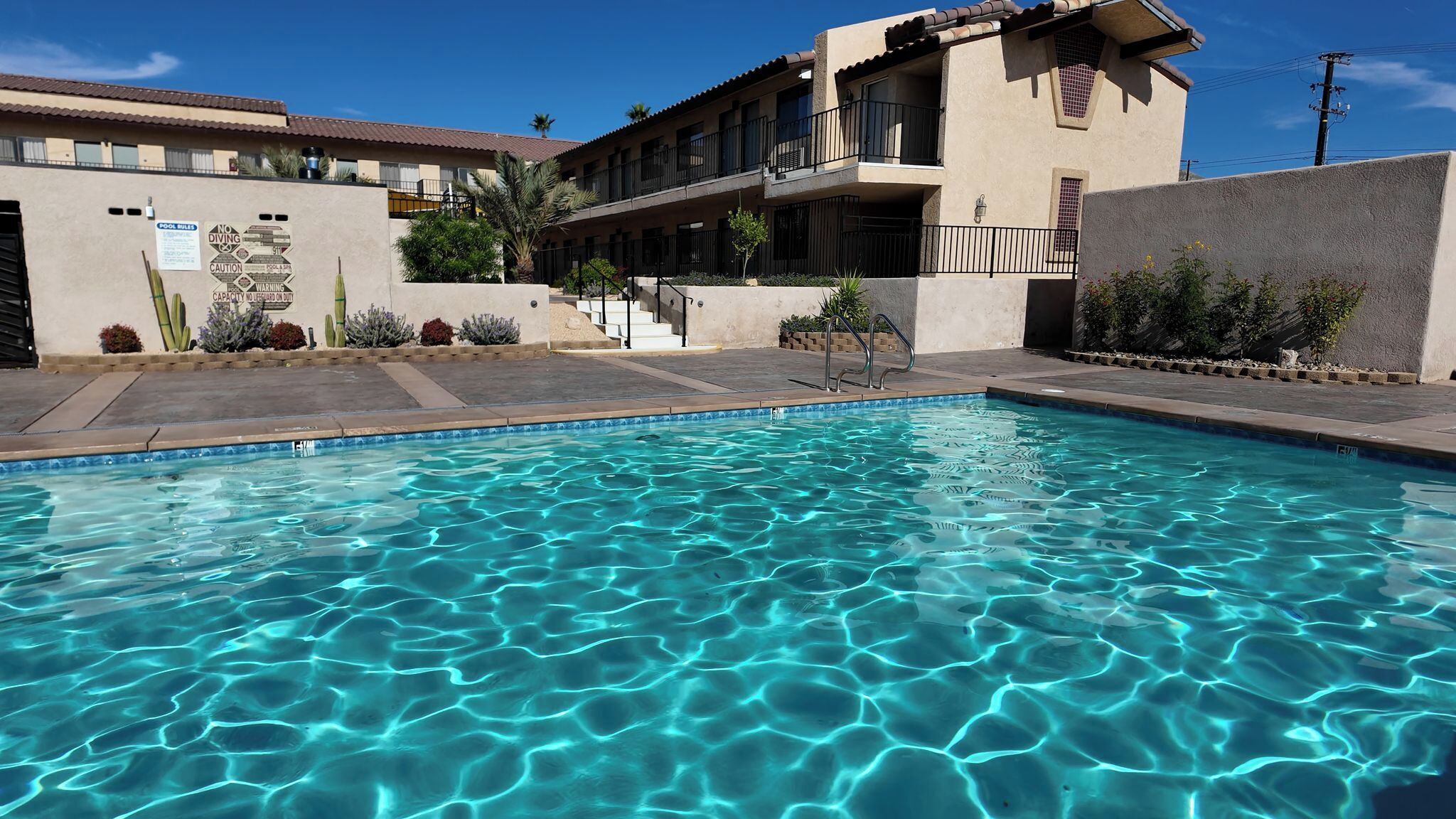 A clear swimming pool with a tiled edge, surrounded by a building with balconies and a stucco exterior.