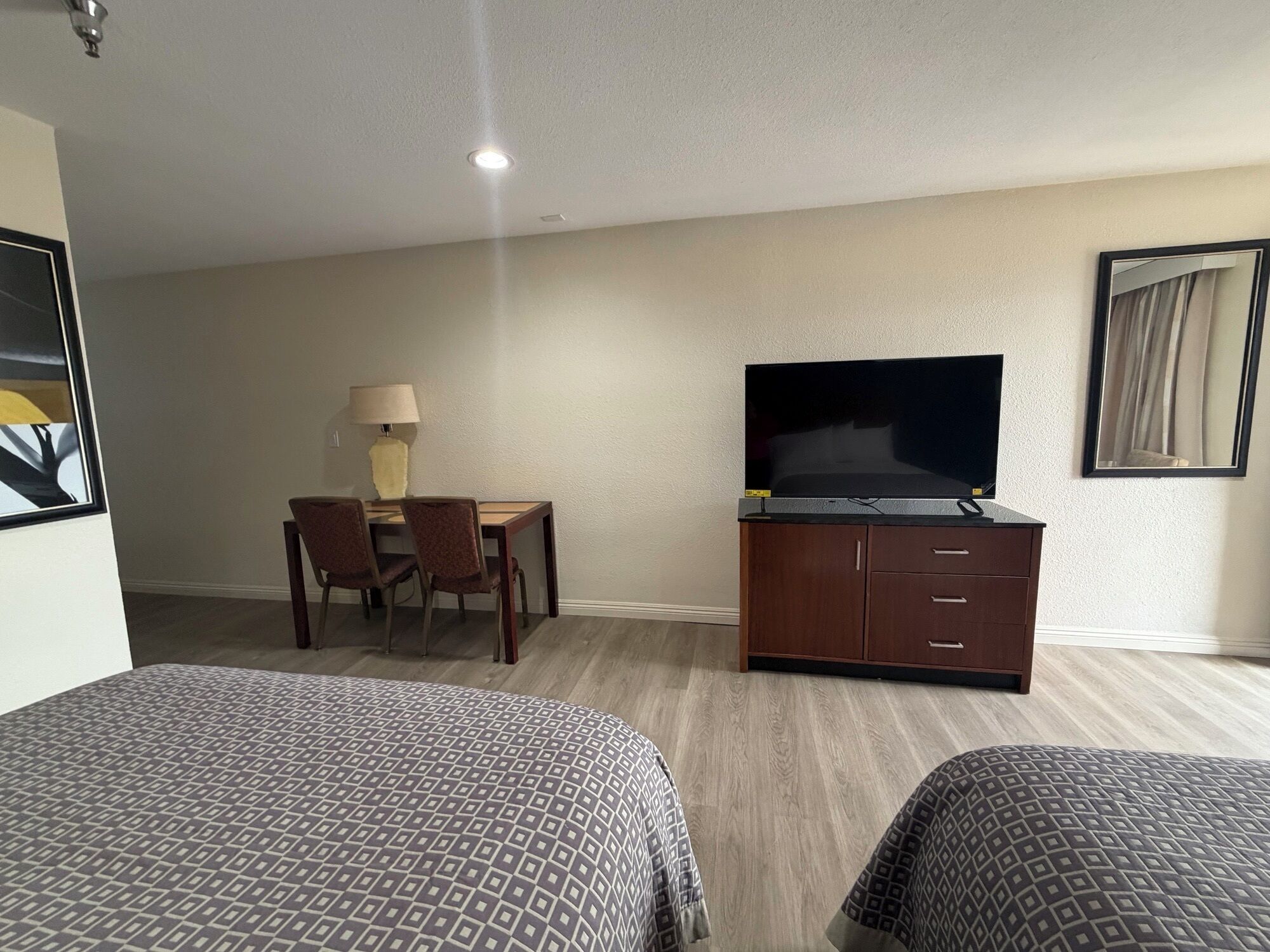 A hotel room with two beds, a TV on a wooden cabinet, a desk with a lamp, and a chair.