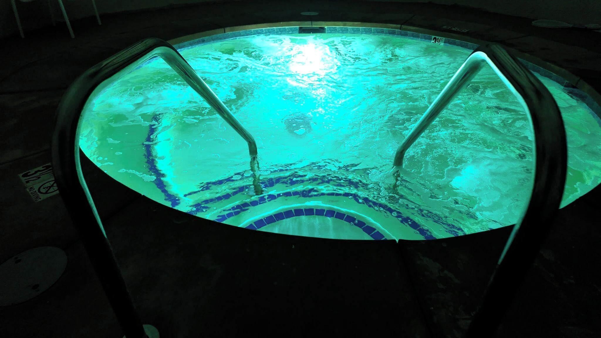Un jacuzzi rond, avec un intérieur carrelé et deux échelles en métal.