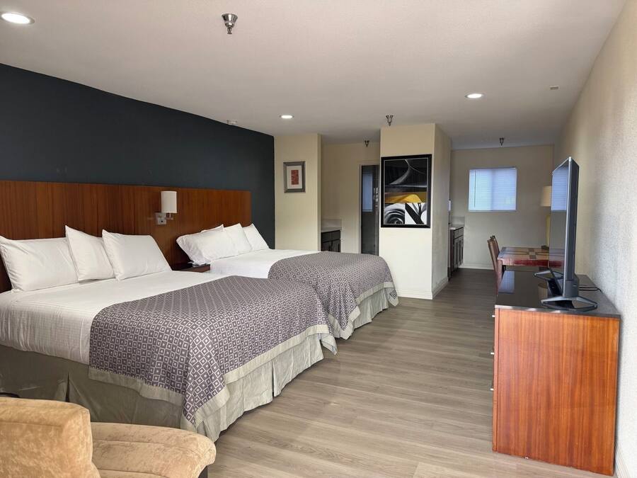 A hotel room with two beds, a desk, a television, and a dining area with a table and chairs.