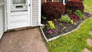 A house with a white door, a brick chimney, and a flower bed with various plants. - Stratford Holiday Home: Perfect for Families (Stratford)