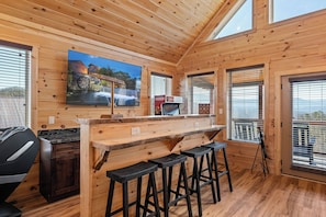 A wooden interior with a bar area, seating, and a large TV screen. - Modern Luxe Cabin w/ Views, Games & Hot Tub (Sevierville)