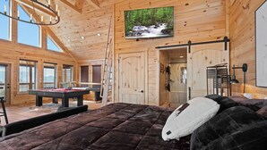 En mysig timmerstuga med en stor säng, ett biljardbord och en tv som är monterad på väggen.