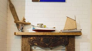 Une cheminée rustique avec une manteau en bois, un coussin rayé aux couleurs vives et, au-dessus, un tableau représentant un paysage marin.