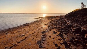 Une plage avec un rivage rocheux et un coucher de soleil en arrière-plan.