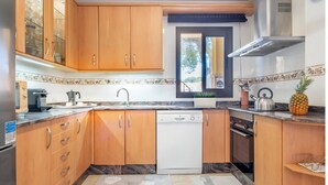 A kitchen with wooden cabinets, a dishwasher, a stove, and a window with a view of trees. - Ca na Kika 1 minute from the best Beaches (Puerto De Alcúdia)