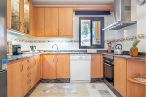 A kitchen with wooden cabinets, a dishwasher, a stove, and a window with a view of trees. - Ca na Kika 1 minute from the best Beaches (Puerto De Alcúdia)