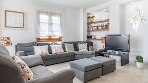 A modern living room with a sectional sofa, ottomans, a flat-screen TV, and decorative shelves. - Ca na Kika 1 minute from the best Beaches (Puerto De Alcúdia)