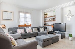 A modern living room with a sectional sofa, ottomans, a flat-screen TV, and decorative shelves. - Ca na Kika 1 minute from the best Beaches (Puerto De Alcúdia)