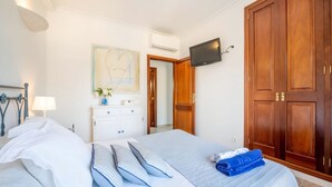 A hotel room with a bed, a TV mounted on the wall, a wardrobe, and a desk with a lamp. - Ca na Kika 1 minute from the best Beaches (Puerto De Alcúdia)