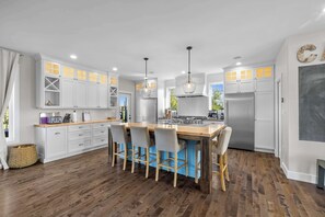 A modern kitchen with white cabinets, a central island with bar stools, a stainless steel refrigerator, and pendant lighting. - Waterfront Home: Slide & Hot Tub (New Glasgow)